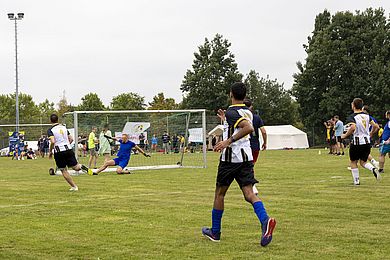 Schuss aufs Tor bei der Liga für ALLE - 3 Spieler in schwarz-weißen Trikots rennen auf das gegnerische Tor zu, der Torwart versucht, den Ball zu halten.