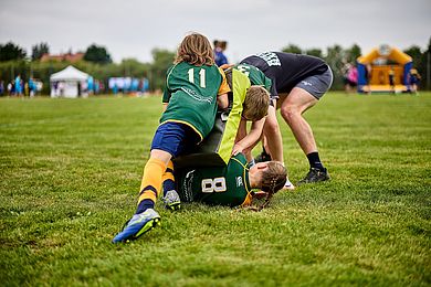 4 Personen beim Rugby beim Kampf um den Ball auf einer Wiese.