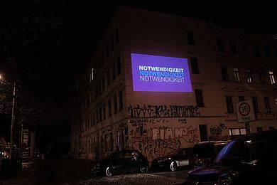 Animationsfilm mit Schlagwort "Notwendigkeit" auf einer Hausfassade