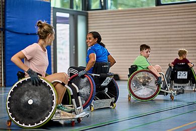 2 Frauen und 2 Kinder in Sport-Rollstühlen in einer Sporthalle