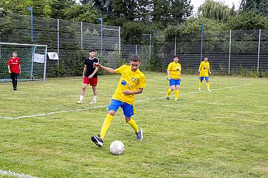 Spieler*innen bei der Liga für ALLE, vorne schießt ein junger Mann in gelb-blauem Trikot den Ball.