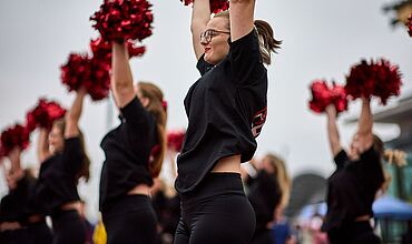 Cheerleaderinnen in schwarzen St-Shirts und roten Puschel.