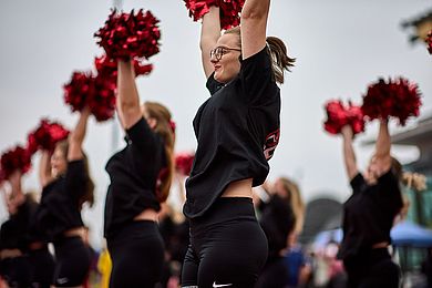 Cheerleaderinnen in schwarzen St-Shirts und roten Puschel.