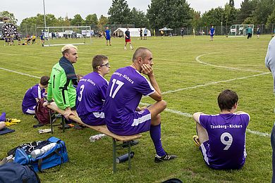 5 Spieler*innen der Thonberg-Kickers warten auf ihren Einsatz am Spielfeldrand. Sie tragen lila Trikots.